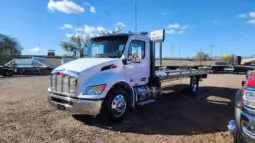 White tow truck parked on gravel lot.