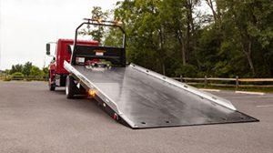 Red flatbed tow truck with its ramp extended on the road.